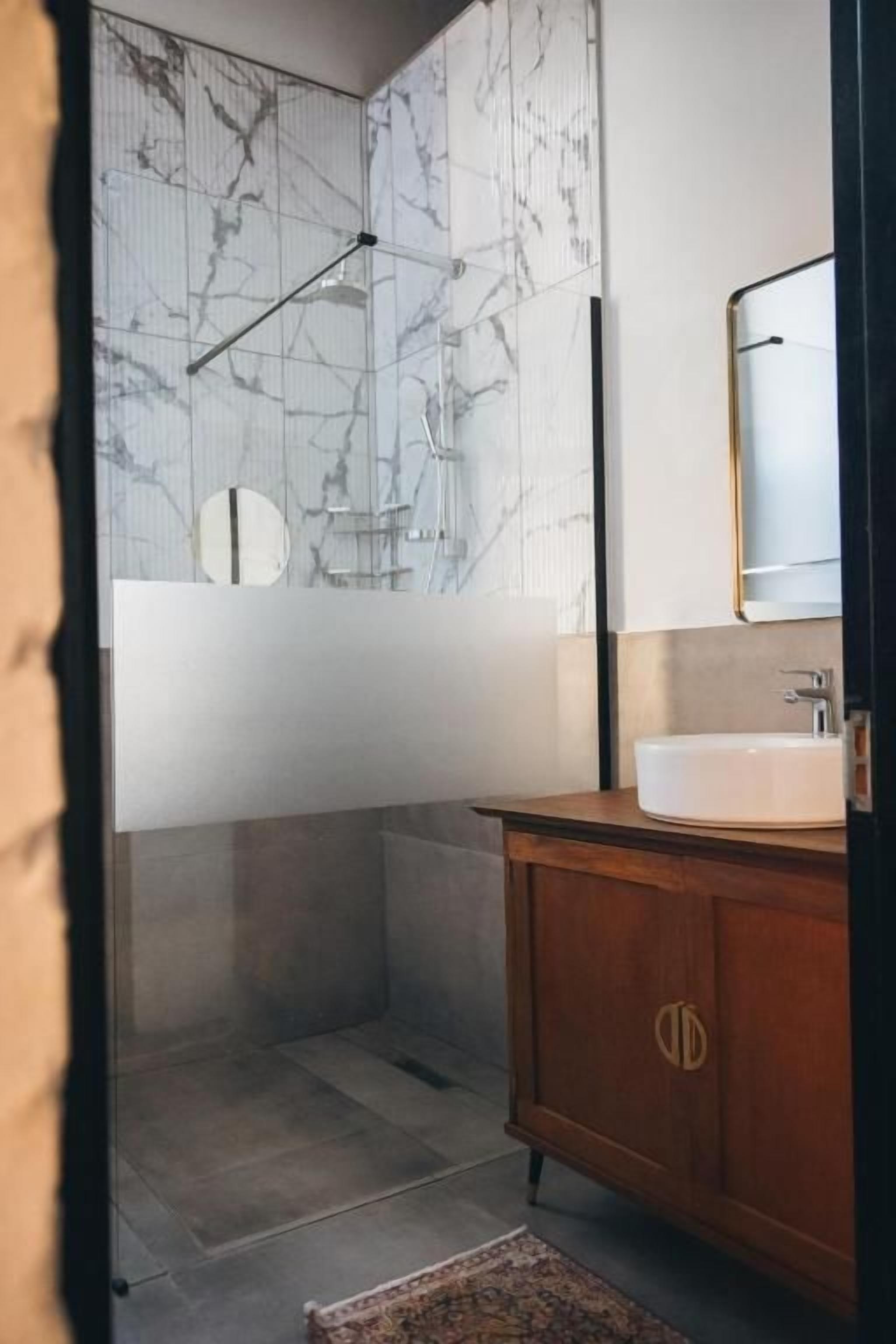 A bathroom with a marble wall, a wooden vanity, and a mirror.