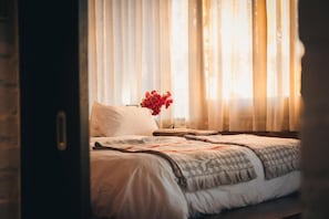 A bedroom with a bed, a nightstand, and a vase of flowers. - studio21 seven (Pretoria)