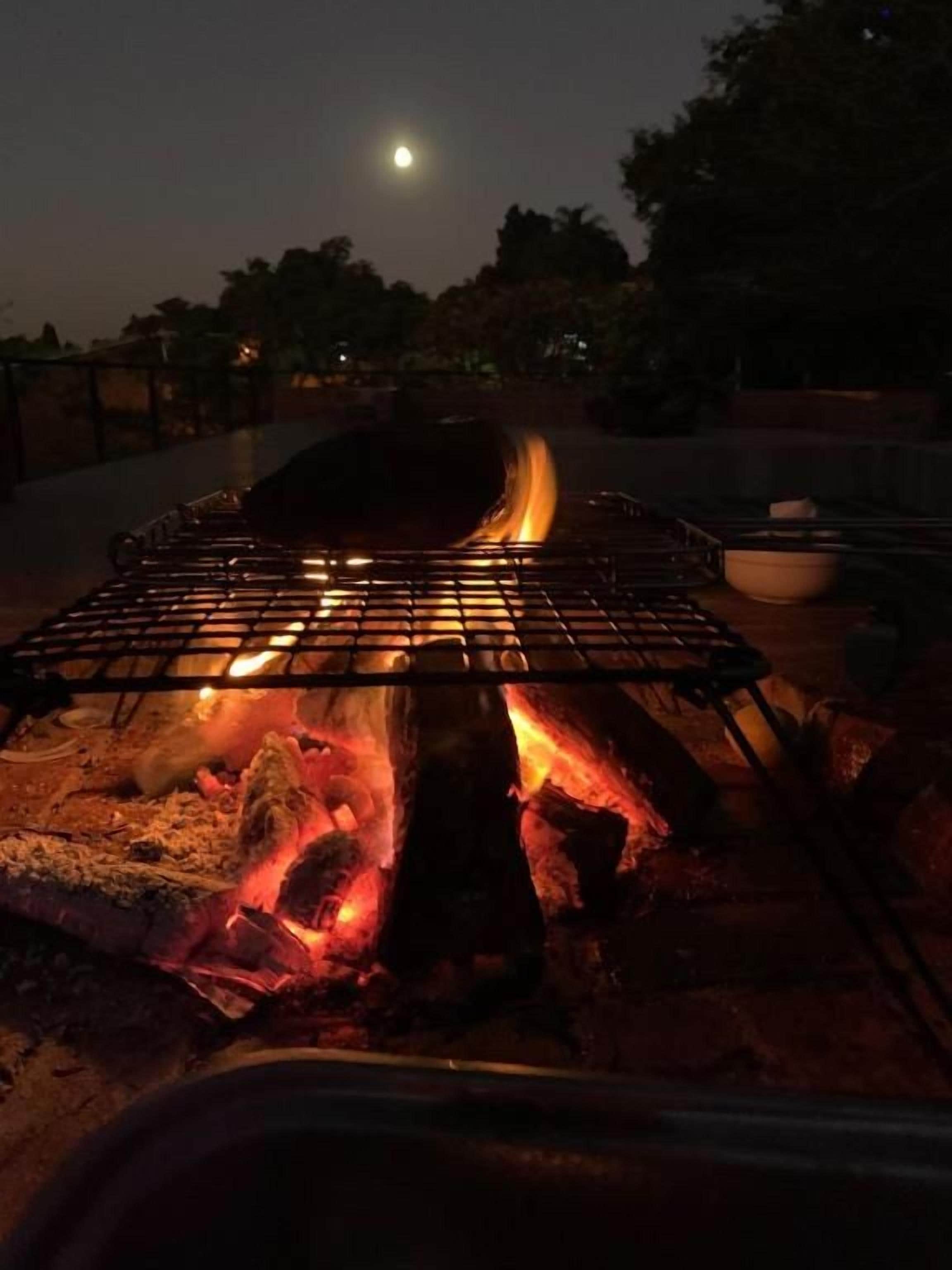 Uma churrasqueira com chamas visíveis e uma tigela ao lado, em ambiente externo à noite.