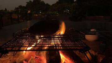 Uma churrasqueira com chamas visíveis e uma tigela ao lado, em ambiente externo à noite.