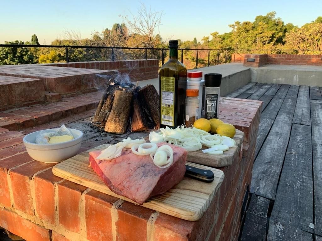 A barbecue setup with meat, onions, lemons, and condiments on a brick surface.