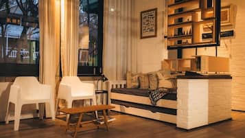 A cozy living room with a sofa, two white chairs, a wooden bench, and a bookshelf.