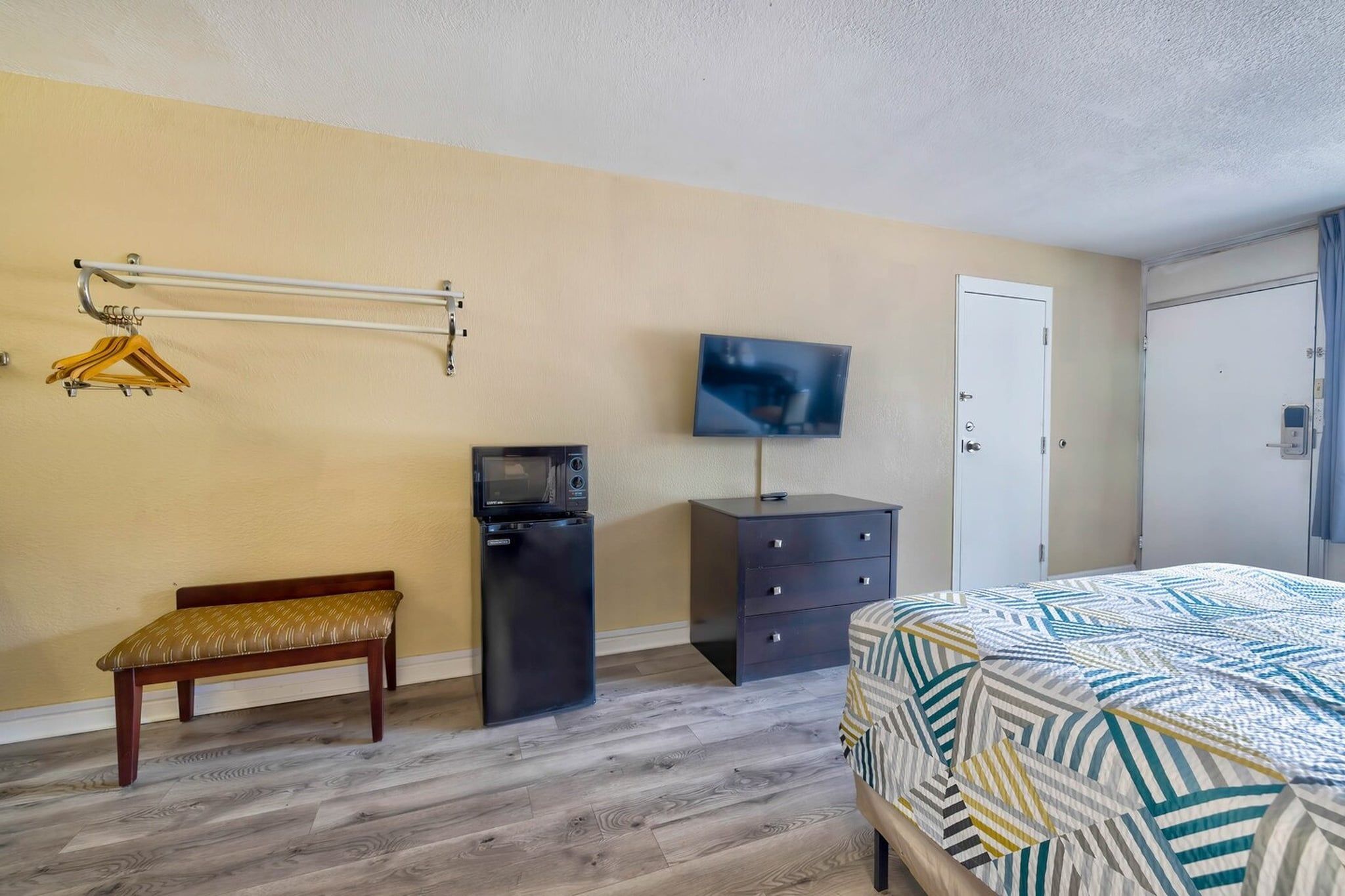 A bedroom with a bed, a TV, a bench, a dresser, and a wardrobe.