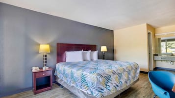 Une chambre d’hôtel avec un lit, deux lampes de chevet, une table de chevet, une chaise bleue et une fenêtre.