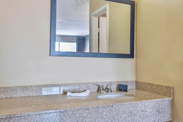 Un baño con encimera de granito, lavamanos, espejo y toalla.