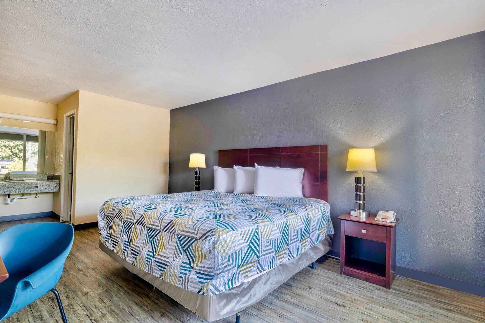 Una habitación de hotel con una cama, dos lámparas de noche, un escritorio con una silla y un ventanal.