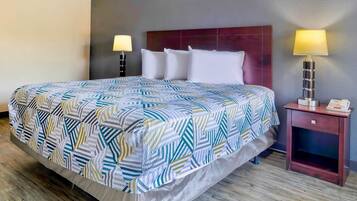 Una habitación de hotel con una cama, dos lámparas de noche, una mesita de noche y piso de madera.
