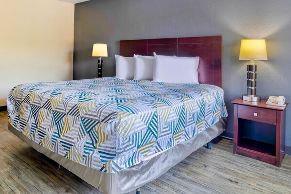 A hotel room with a bed, two bedside lamps, a nightstand, and a wooden floor.