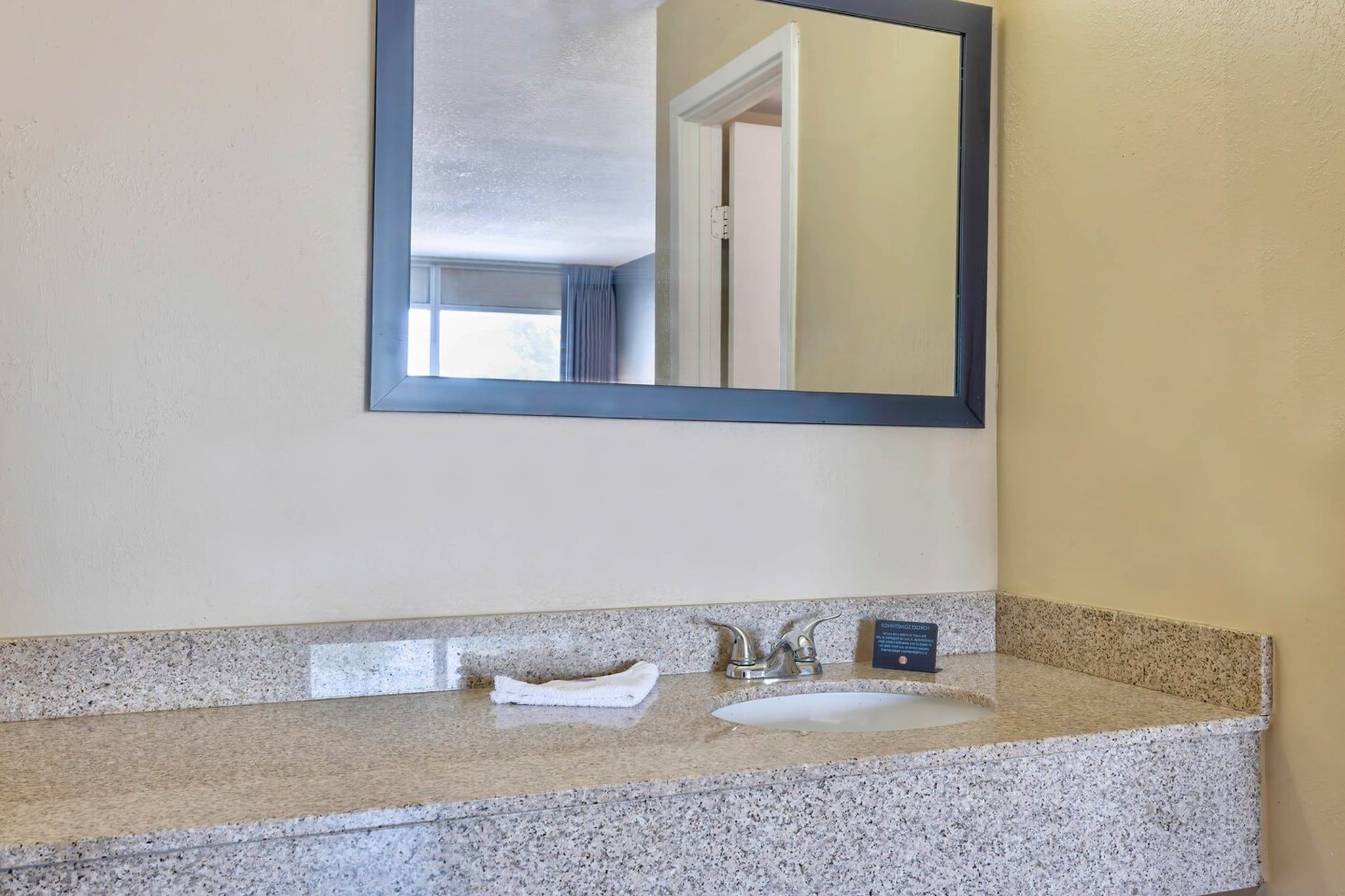 A bathroom with a granite countertop, a sink, a mirror, and a towel.
