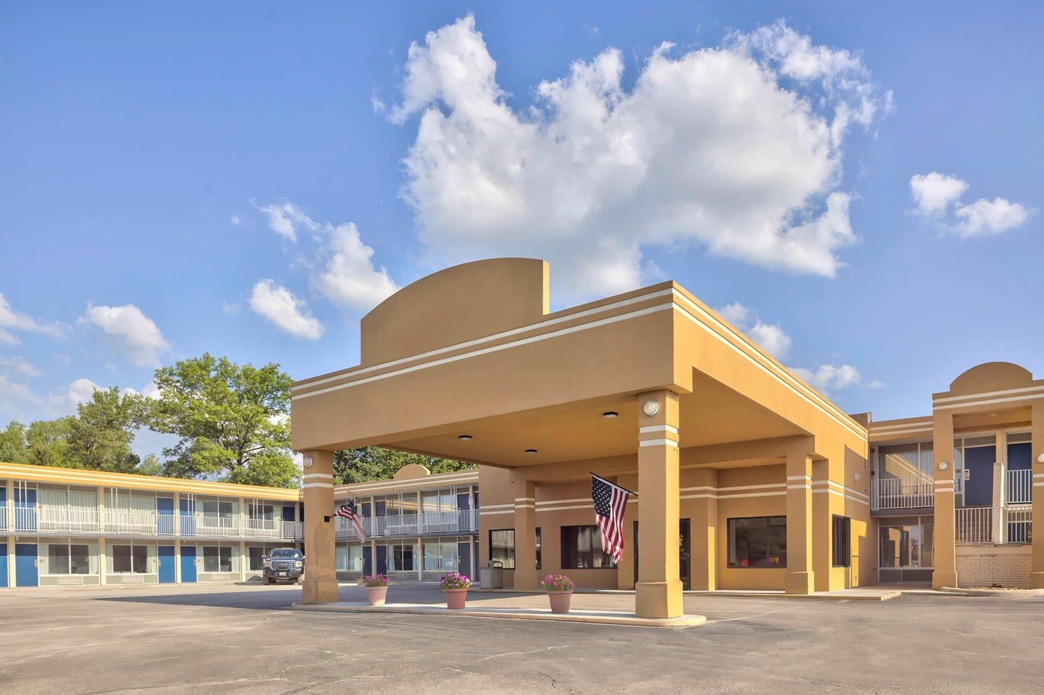 A motel with a covered parking area, multiple rooms, and an American flag.