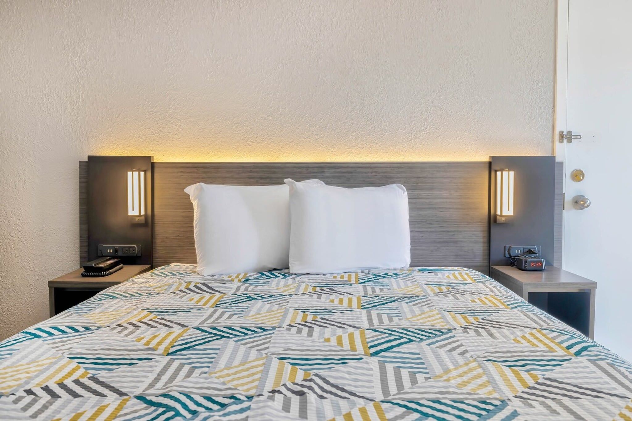 A hotel room with a bed, two bedside tables, and wall-mounted lamps.