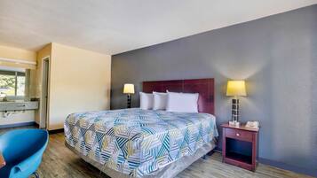 Quarto de hotel com cama, duas luminárias de cabeceira, escrivaninha e cadeira, e uma janela.