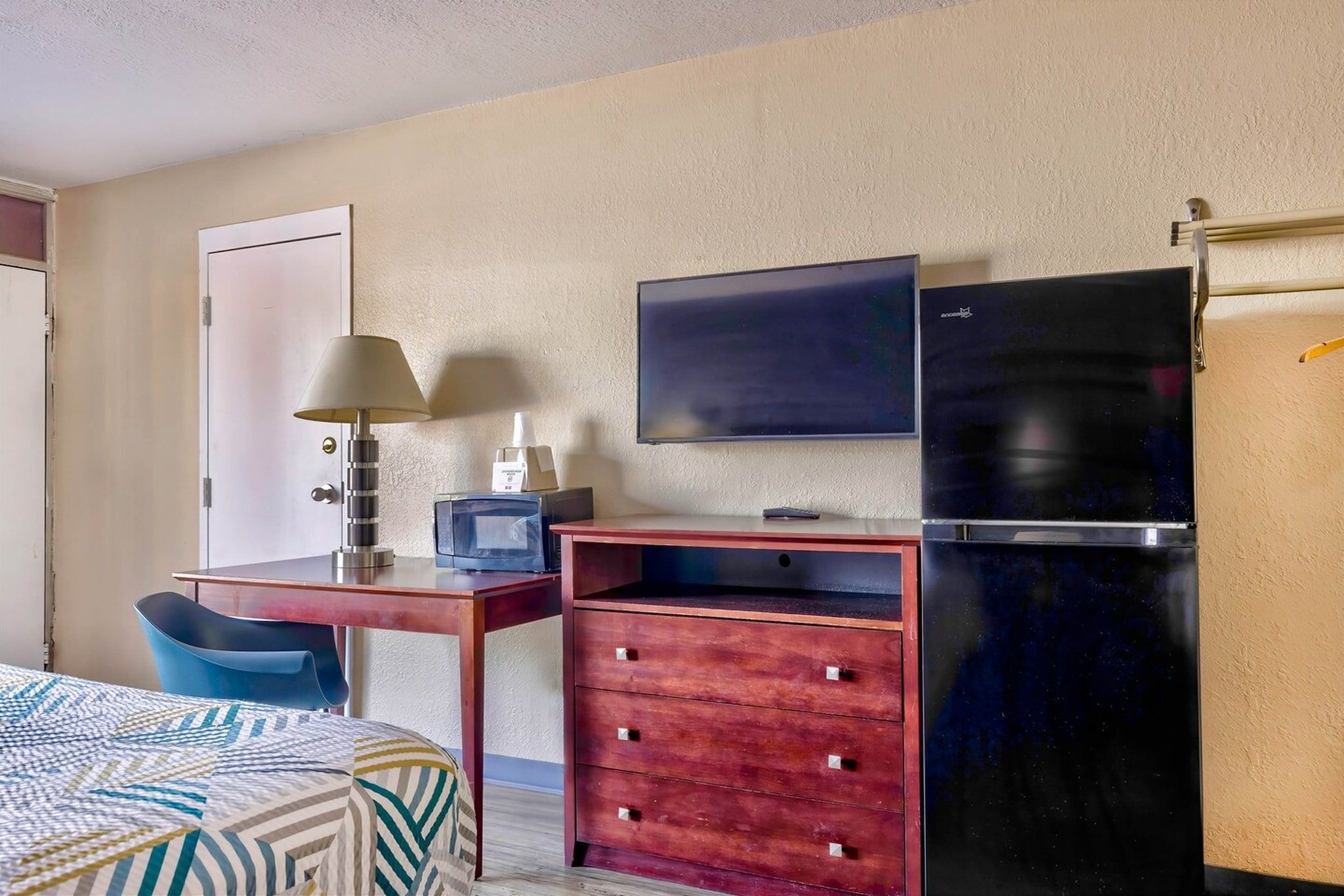 Une chambre d’hôtel comprenant un lit, un bureau avec une lampe, une télévision, un réfrigérateur et une armoire.