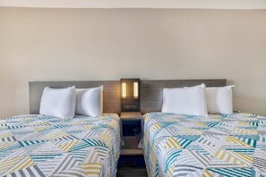 A hotel room with two beds, each with a patterned bedspread, a nightstand with a lamp, and a wall-mounted light fixture.
