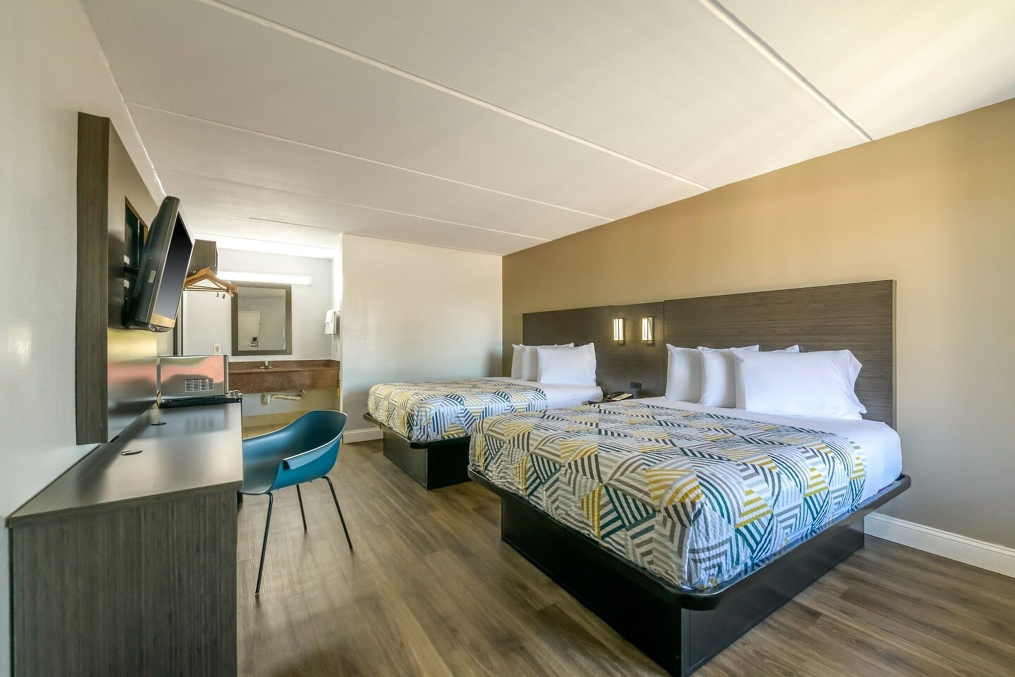 Habitación de hotel con dos camas, un escritorio, una silla, un televisor y un espejo.