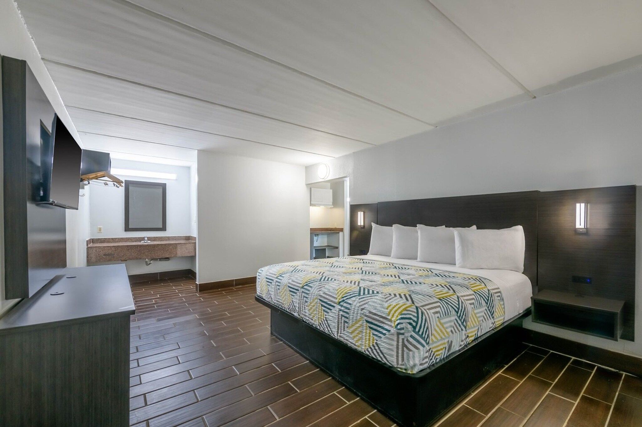 Une chambre d’hôtel moderne dotée d’un grand lit, d’un téléviseur à écran plat, d’un bureau intégré et d’une petite kitchenette.
