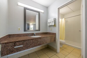 A bathroom with a granite countertop sink, a mirror, a shower with a yellow curtain, and a toilet. - 1 King Bed | Smoking, Kitchen (Stockbridge GA)