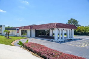 Un hôtel avec un toit recouvert de tuiles rouges, une entrée abritée et un parking.