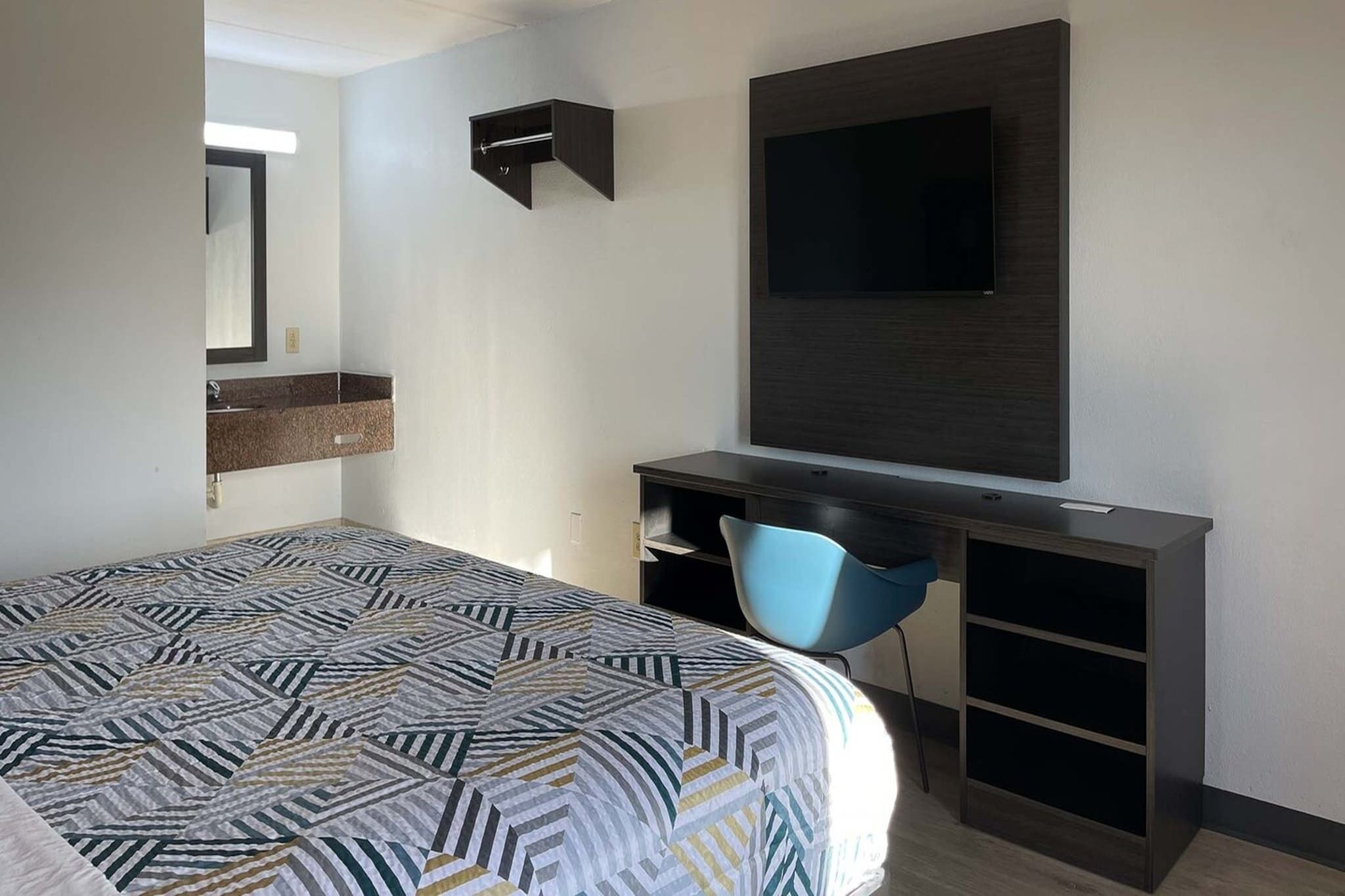 Habitación de hotel con cama, escritorio con silla, televisor y estante empotrado.
