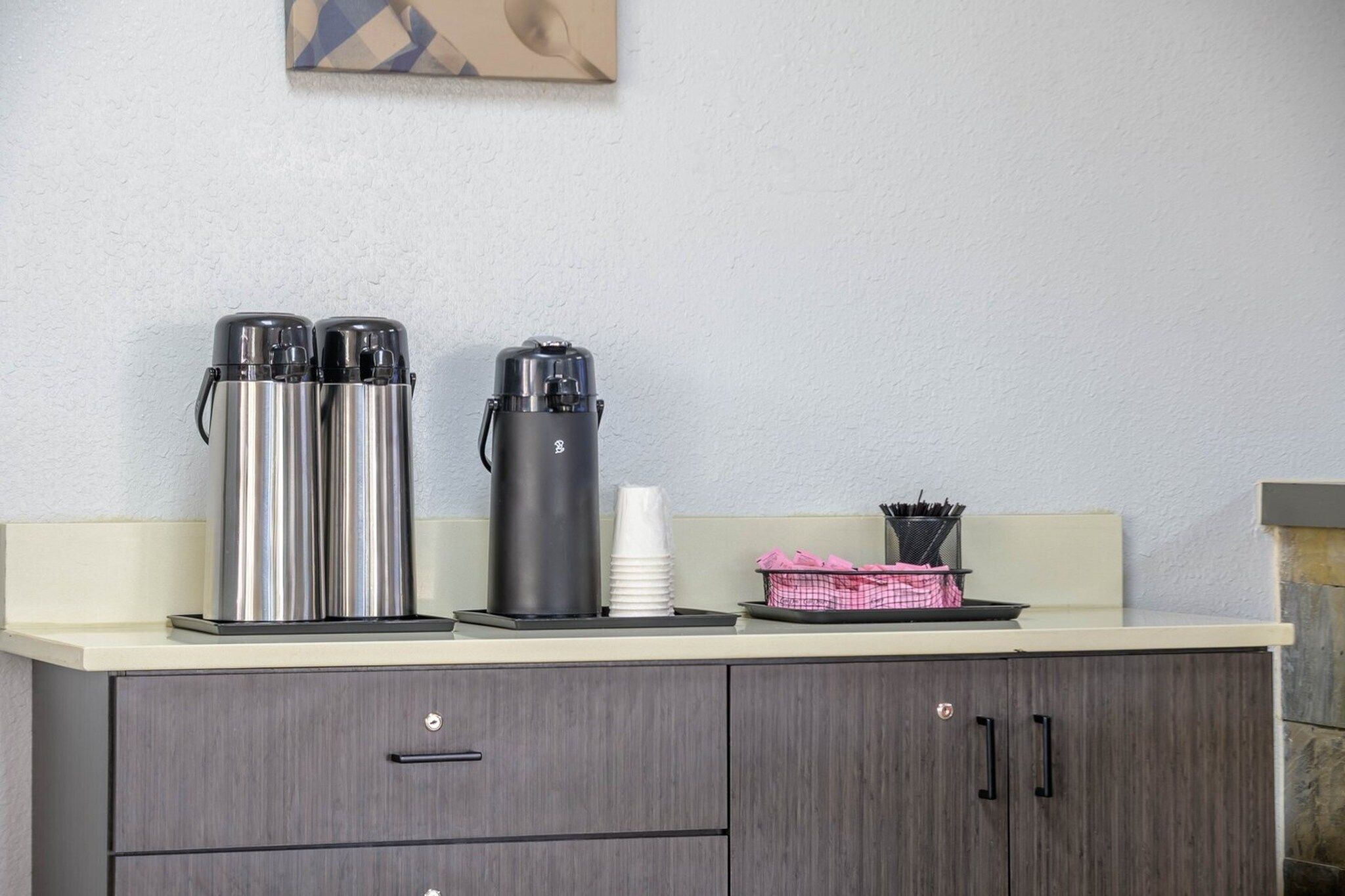 A kitchenette with stainless steel coffee makers, a white cup, and a basket with utensils.