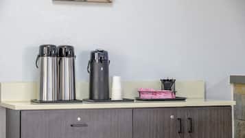 A kitchenette with stainless steel coffee makers, a white cup, and a basket with utensils.