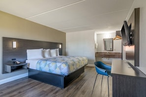 Habitación de hotel con cama, escritorio, silla, televisión y baño visible a través de una puerta abierta.