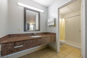 Un baño con encimera de granito, un lavabo, un espejo, una ducha con cortina amarilla y un inodoro.