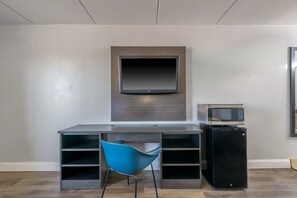 Een moderne kamer met een flatscreen televisie aan de muur, een bureau met stoel, en een kleine zwarte koelkast.