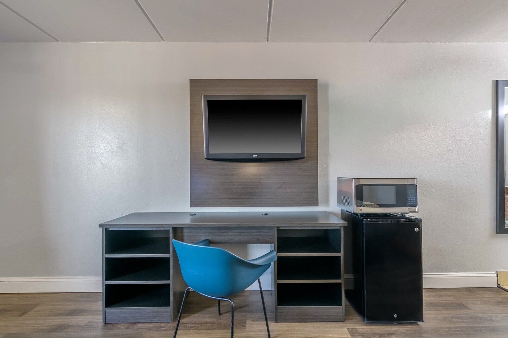 Una habitación moderna con una televisión de pantalla plana en la pared, un escritorio con una silla y un mueble negro pequeño.