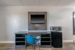 A modern room with a flat-screen TV mounted on the wall, a desk with a chair, and a small black cabinet.