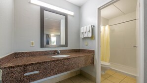 Un bany amb taulell de granit, un lavabo, un mirall, una dutxa amb cortina groga i un vàter.