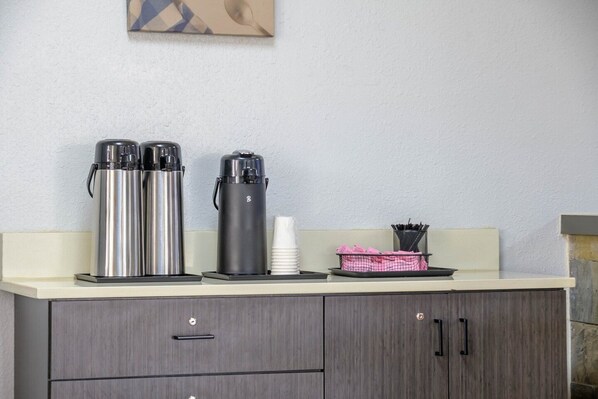 A kitchenette with stainless steel coffee makers, a white cup, and a basket with utensils.
