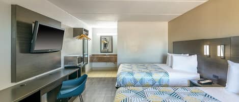 A hotel room with a TV, a desk, a microwave, a bed with patterned bedding, and a bedside table with a phone.