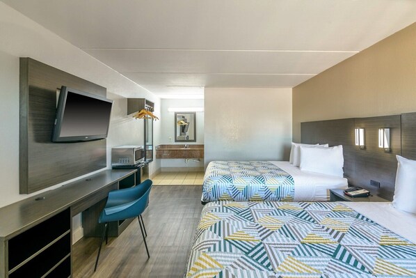 A hotel room with a TV, a desk, a microwave, a bed with patterned bedding, and a bedside table with a phone. - 2 Queen Beds | Non-Smoking, Kitchen (Stockbridge GA)