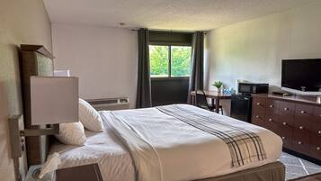 A hotel room with a bed, a desk, a television, and a window with curtains.