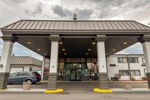 Un edificio con un acceso cubierto, columnas y un coche estacionado al frente.