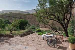 A patio with stone flooring, a table with chairs, and potted plants.