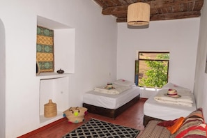 A room with two beds, a hanging light fixture, a window with a view, and a woven basket.