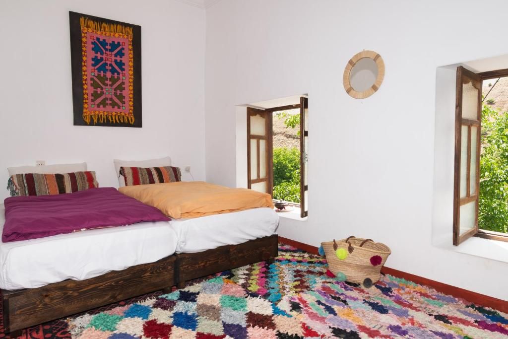 Une chambre avec un lit, un tapis coloré, une fenêtre ouverte et une décoration murale.