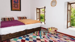 A bedroom with a bed, colorful rug, open window, and a wall hanging. - aubrege sremt (Sremt)