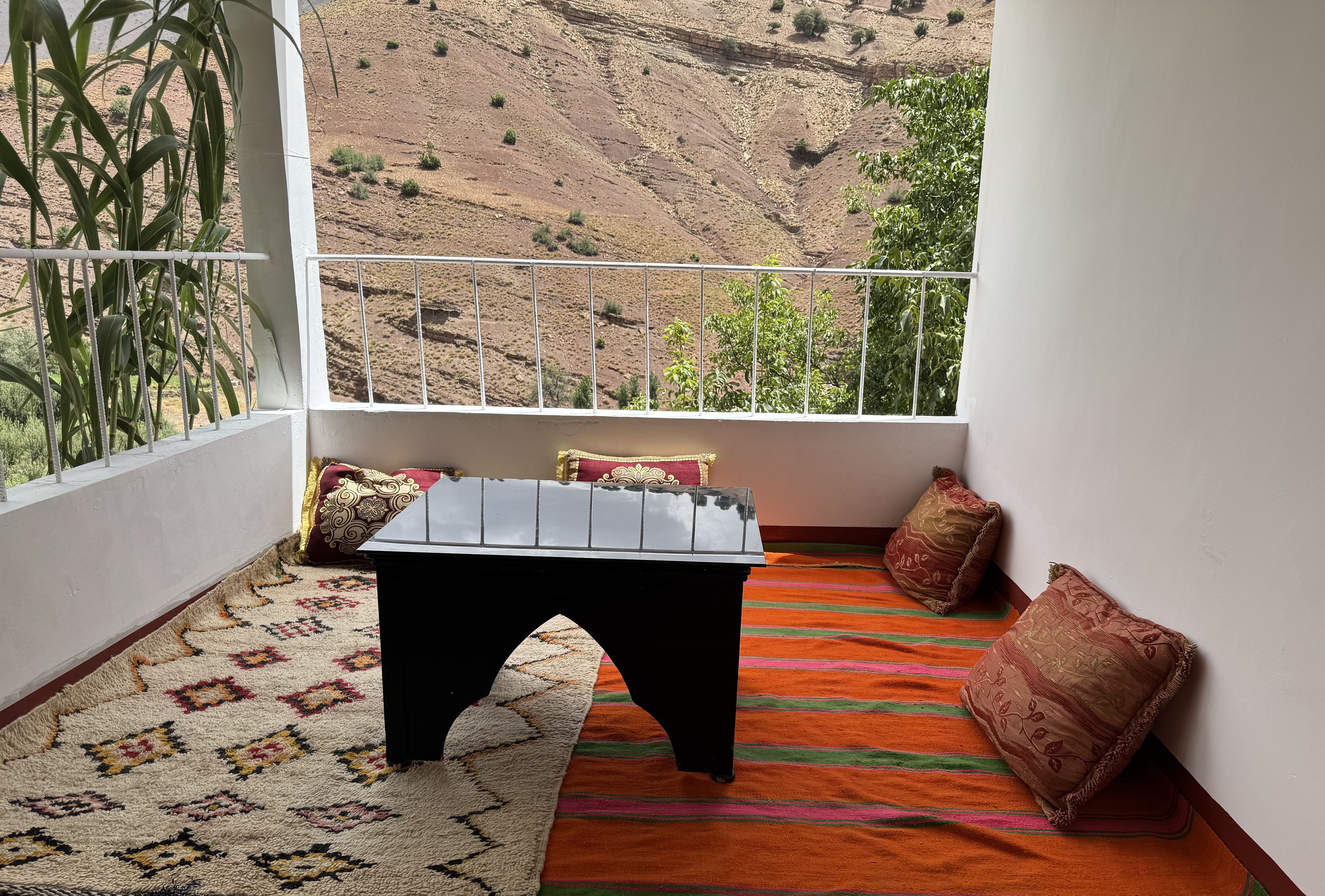 Un balcón con vistas a un paisaje montañoso, una pequeña mesa y una alfombra estampada.