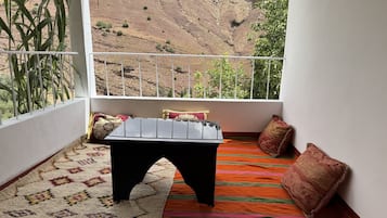 Un balcón con vistas a un paisaje montañoso, una pequeña mesa y una alfombra estampada.