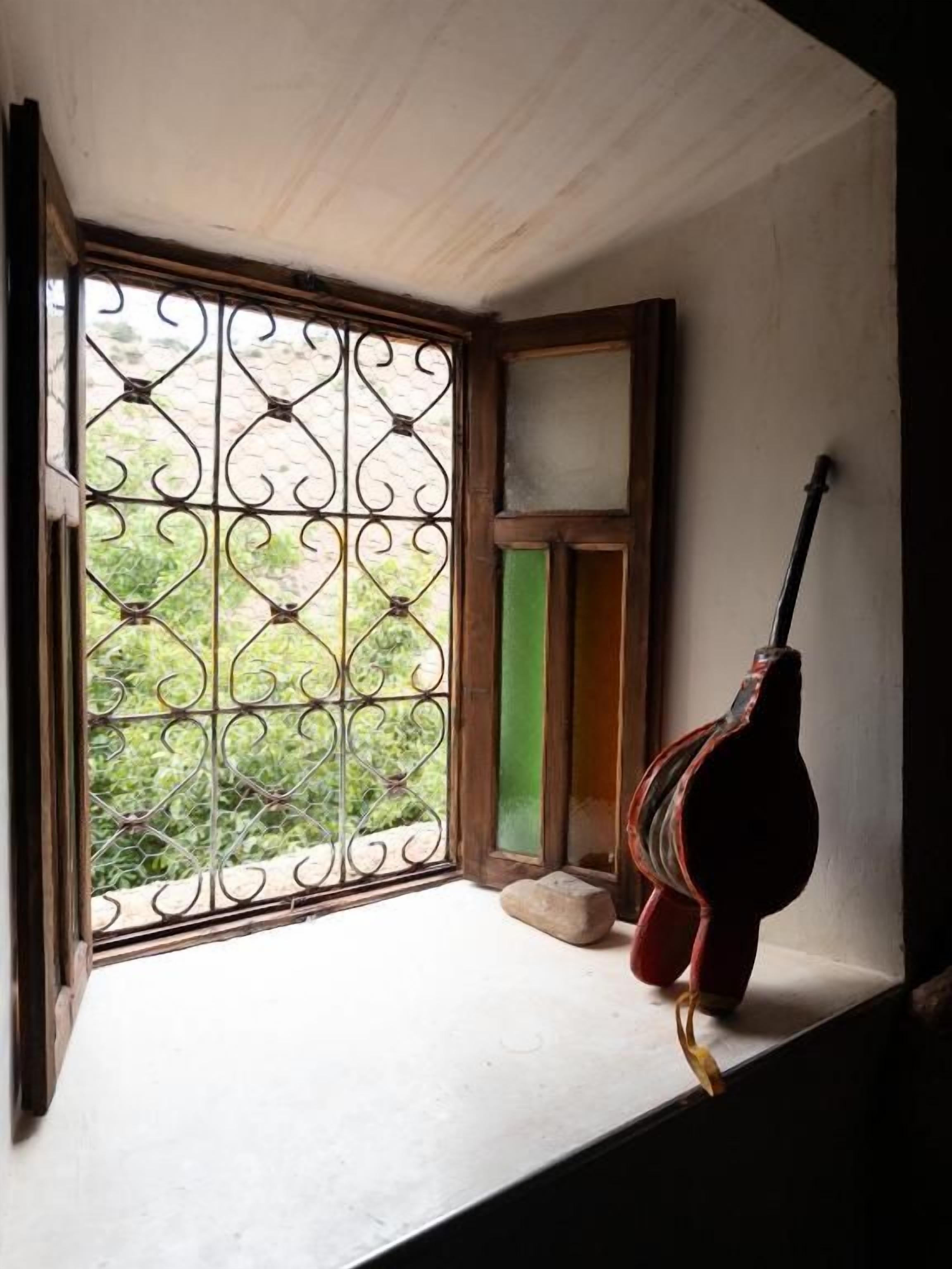 A window with a decorative metal grille and a guitar leaning against the window sill.