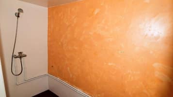 Et badeværelse med en bruser, en hvid væg og en væg med orange struktur.