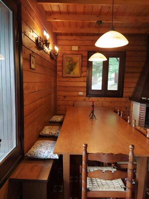 A wooden interior with a long dining table, benches, and a fireplace.
