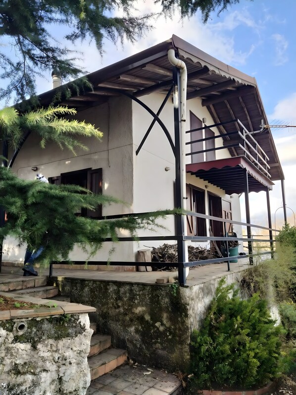 A building with a sloped roof, a staircase leading to a porch, and a large tree in the foreground.