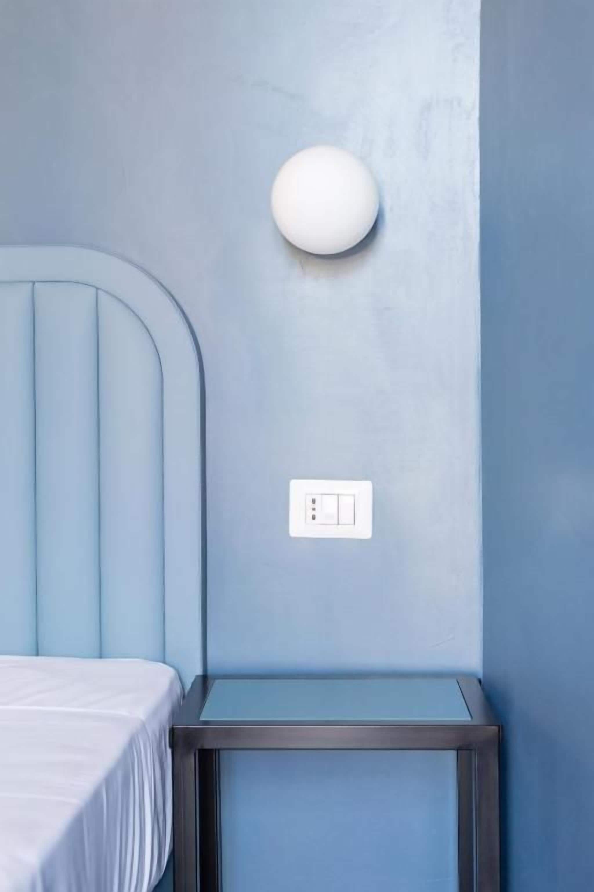 A room with a bed, a bedside table, a wall-mounted light, and a switch.