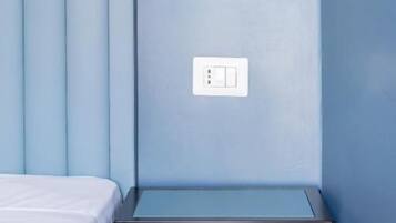 Une chambre avec un lit, une table de chevet, une lampe fixée au mur et un interrupteur.
