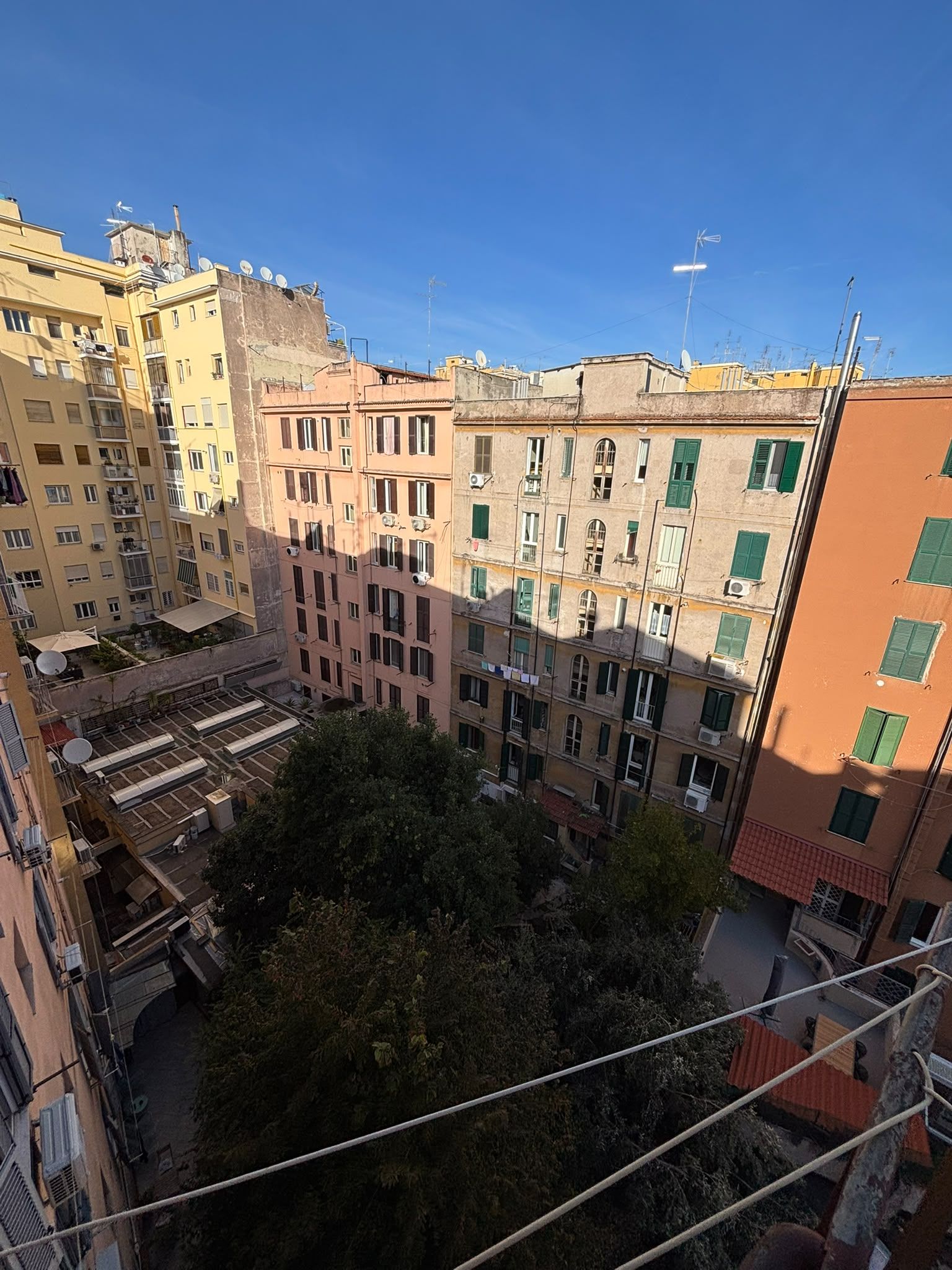 A multi-story residential building with balconies, satellite dishes, and a clear sky.