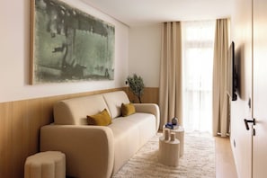 Ein modernes Wohnzimmer mit einem beigefarbenen Sofa, einem Couchtisch, einem großen abstrakten Gemälde, einer Topfpflanze und einer Tür mit einem aufgehängten Mantel.